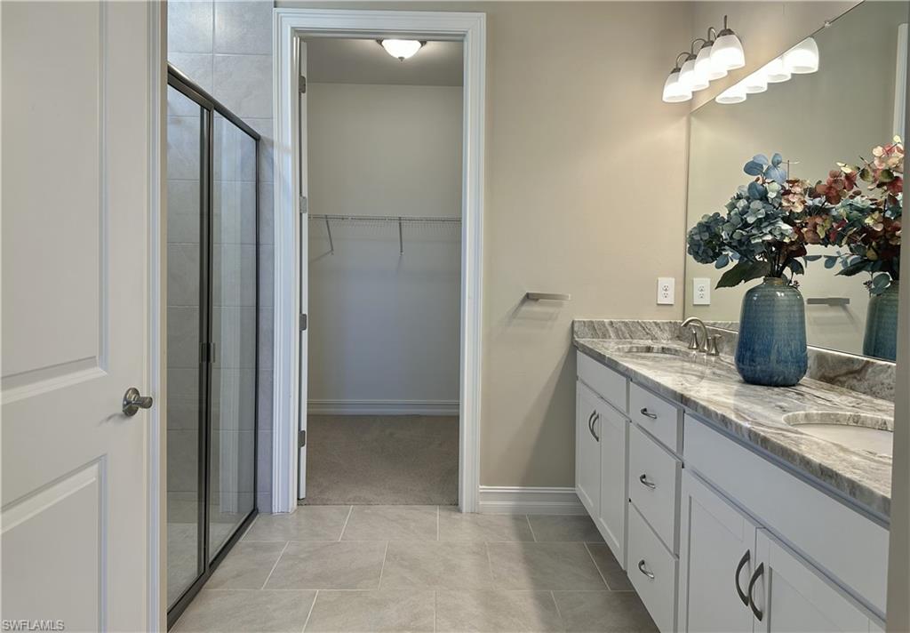 Bathroom with double vanity, light tile patterned flooring, a walk in closet, and a shower stall