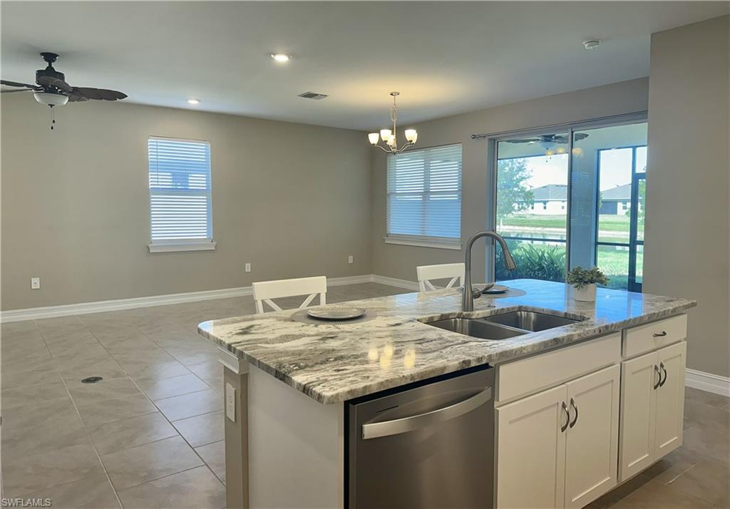 Kitchen with stainless steel dishwasher, white cabinets, light stone countertops, ceiling fan, and pendant lighting
