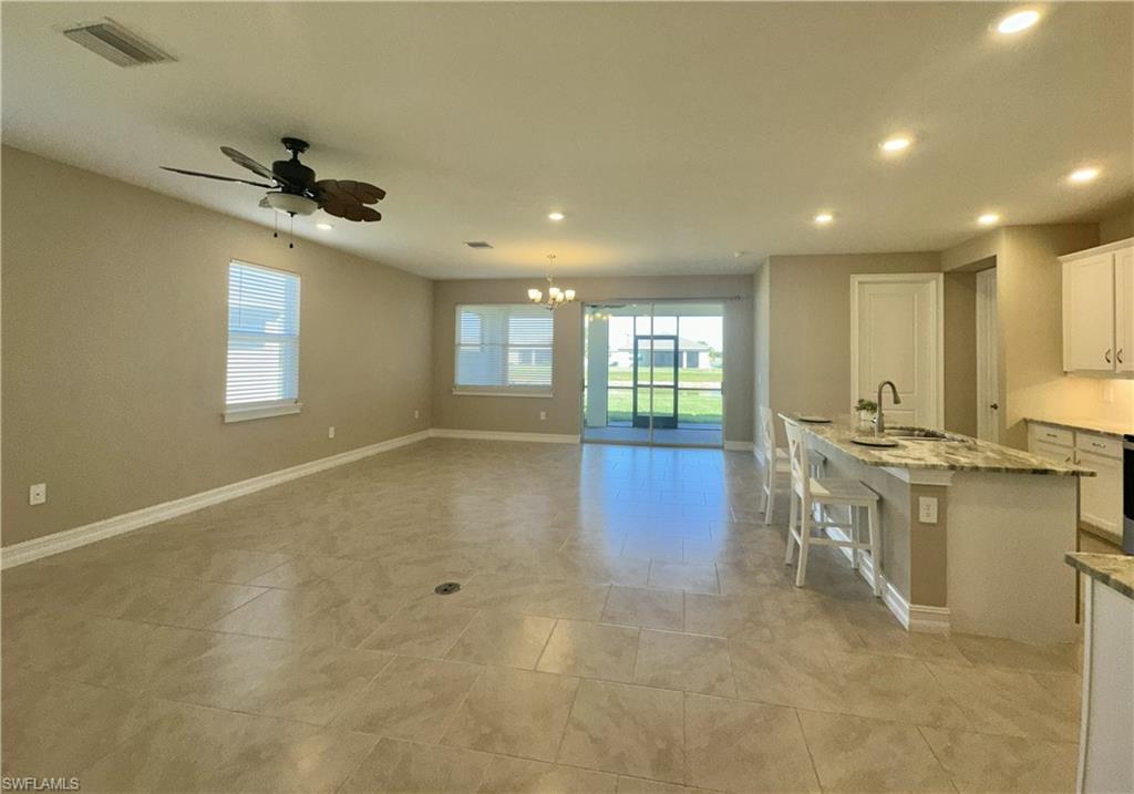 Kitchen with white cabinets, light stone counters, a center island with sink, recessed lighting, and a kitchen bar
