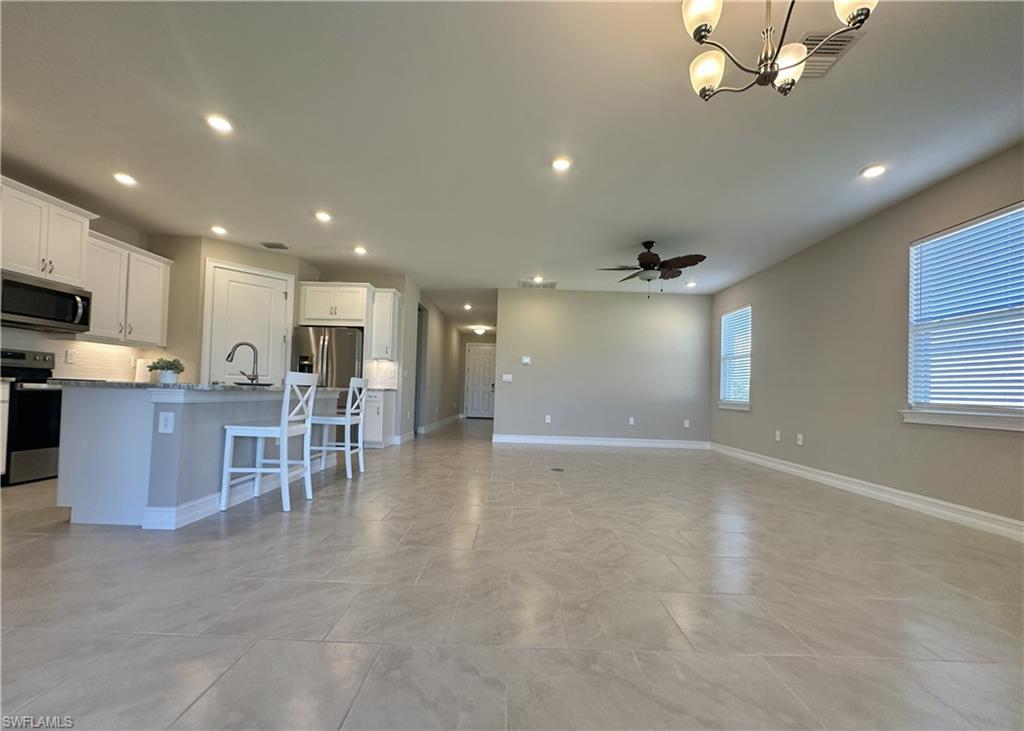 Kitchen with stainless steel appliances, a kitchen island with sink, a breakfast bar area, white cabinetry, and recessed lighting