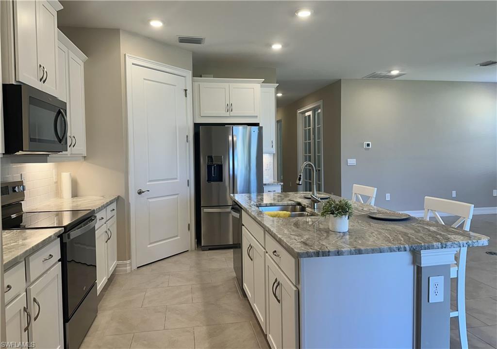 Kitchen featuring black appliances, a kitchen breakfast bar, white cabinets, light stone countertops, and recessed lighting