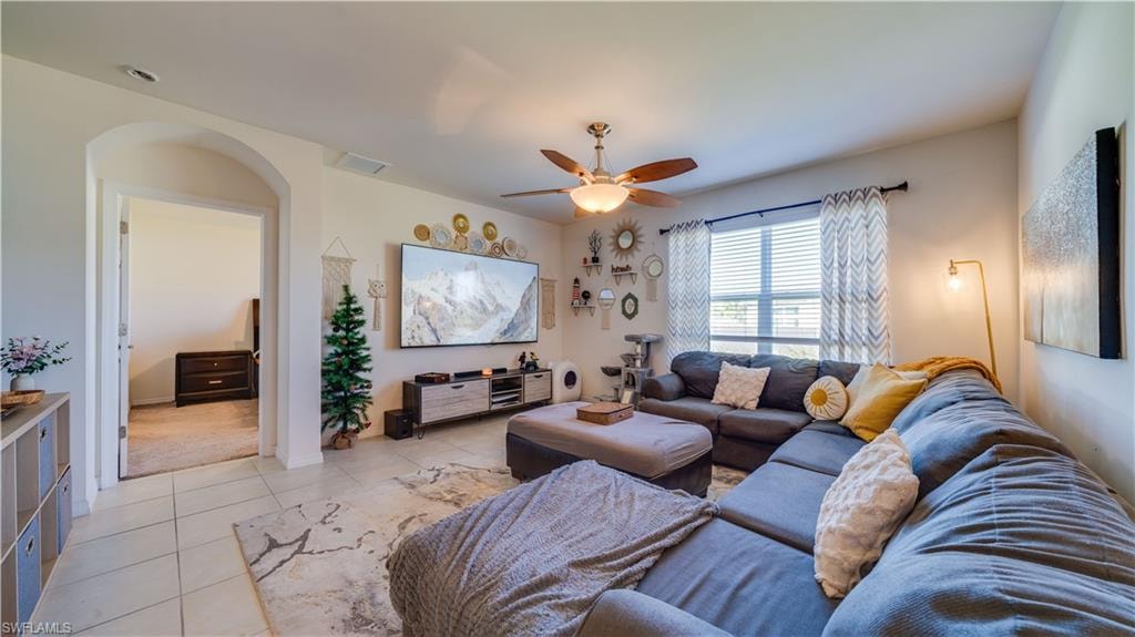 Living area with light tile patterned floors, ceiling fan, and arched walkways