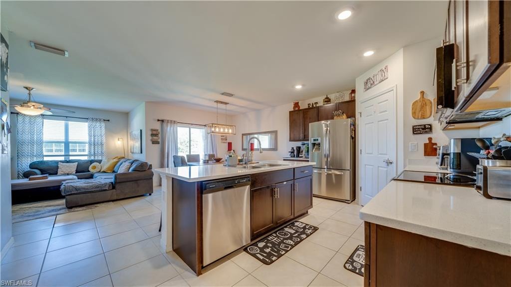 Kitchen featuring black appliances, open floor plan, hanging light fixtures, dark brown cabinets, and light tile patterned floors