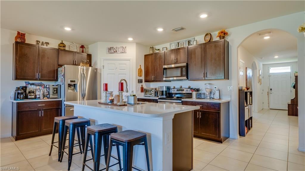 Kitchen featuring a breakfast bar area, light tile patterned floors, arched walkways, recessed lighting, and stainless steel appliances