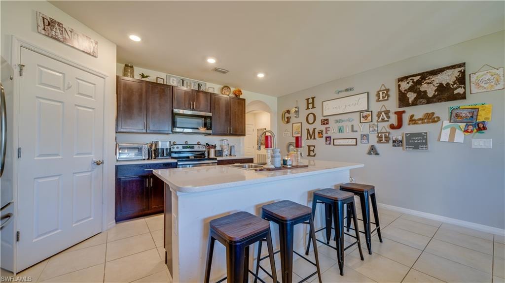 Kitchen featuring a kitchen breakfast bar, dark brown cabinetry, a kitchen island with sink, light tile patterned floors, and recessed lighting