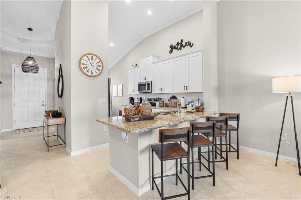 Kitchen with white cabinetry, light stone counters, a breakfast bar area, pendant lighting, and a peninsula
