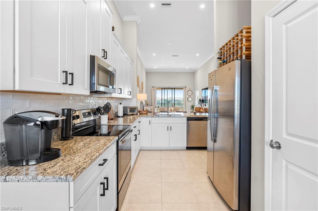 Kitchen featuring appliances with stainless steel finishes, white cabinets, light stone countertops, light tile patterned floors, and recessed lighting
