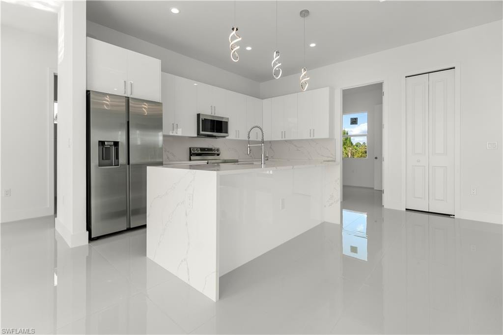 Kitchen with appliances with stainless steel finishes, white cabinetry, light stone countertops, decorative light fixtures, and recessed lighting