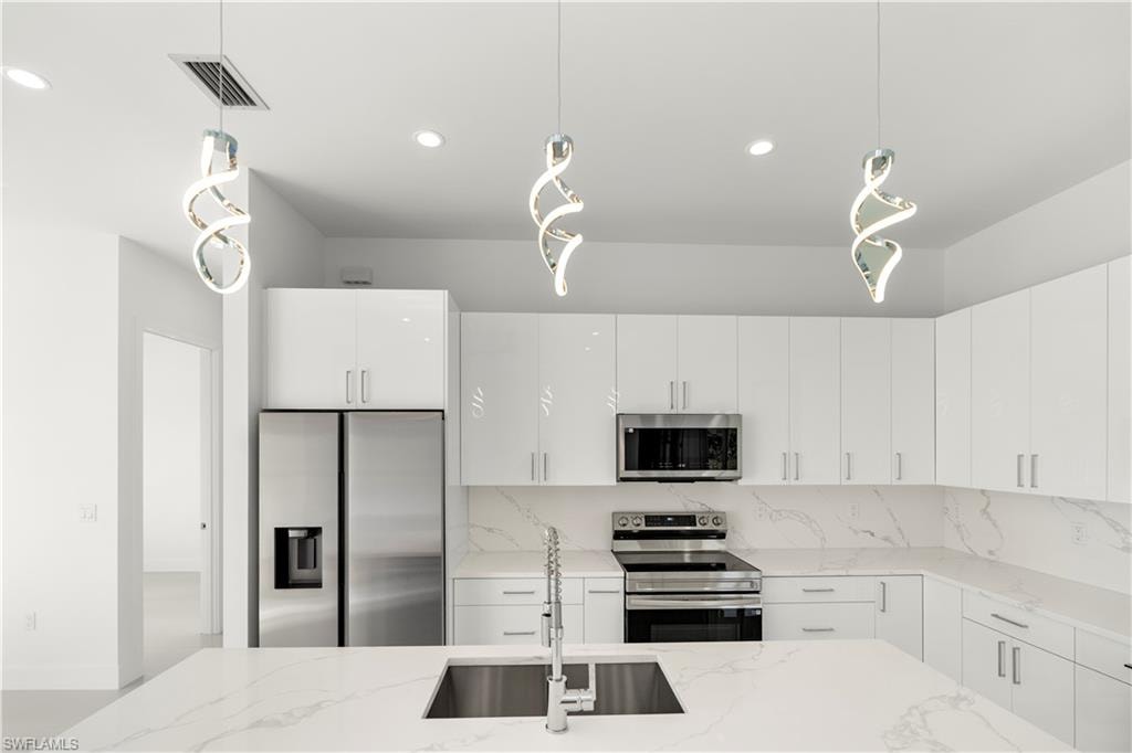 Kitchen featuring hanging light fixtures, appliances with stainless steel finishes, light stone counters, modern cabinets, and white cabinets