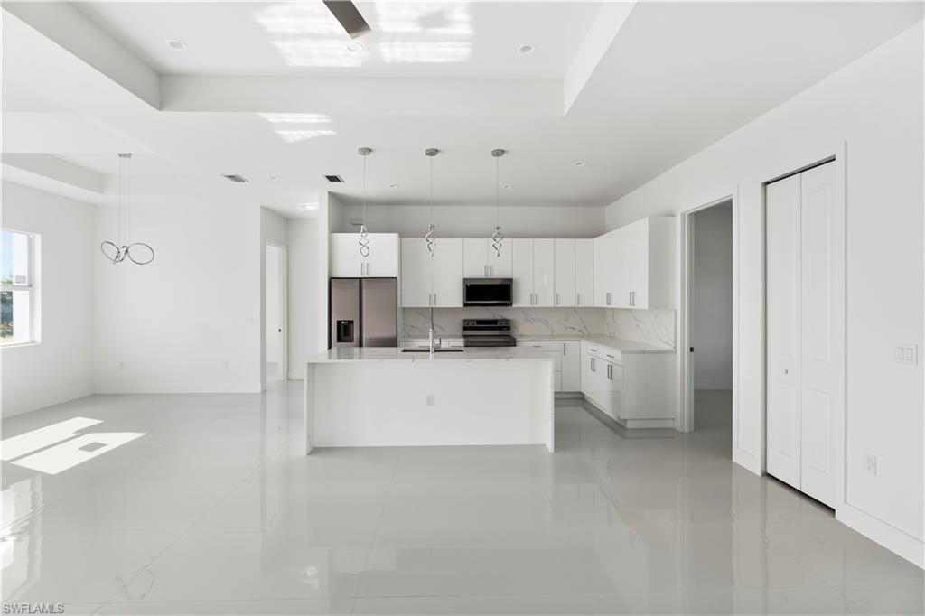 Kitchen with white cabinetry, hanging light fixtures, stainless steel appliances, a center island with sink, and a tray ceiling