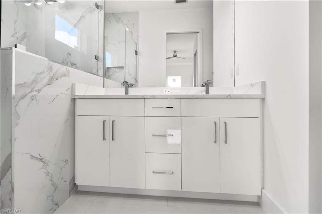Bathroom featuring double vanity, a marble finish shower, and a ceiling fan