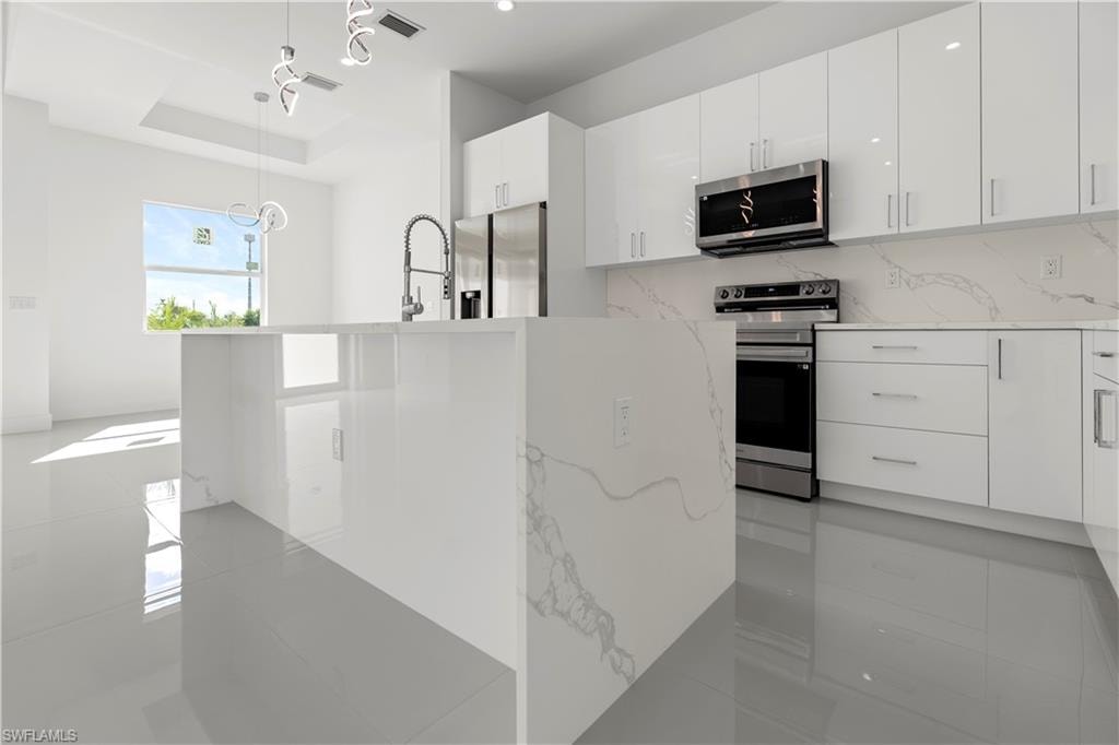Kitchen featuring appliances with stainless steel finishes, light stone counters, modern cabinets, and white cabinets