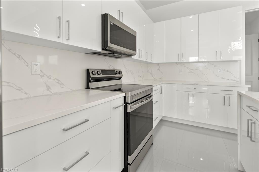 Kitchen featuring stainless steel appliances, backsplash, modern cabinets, white cabinetry, and light stone countertops