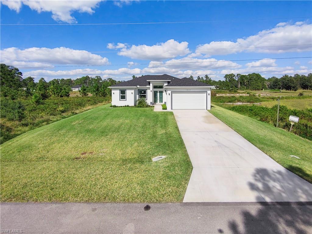 Prairie-style home featuring concrete driveway, a front yard, an attached garage, and view of scattered trees