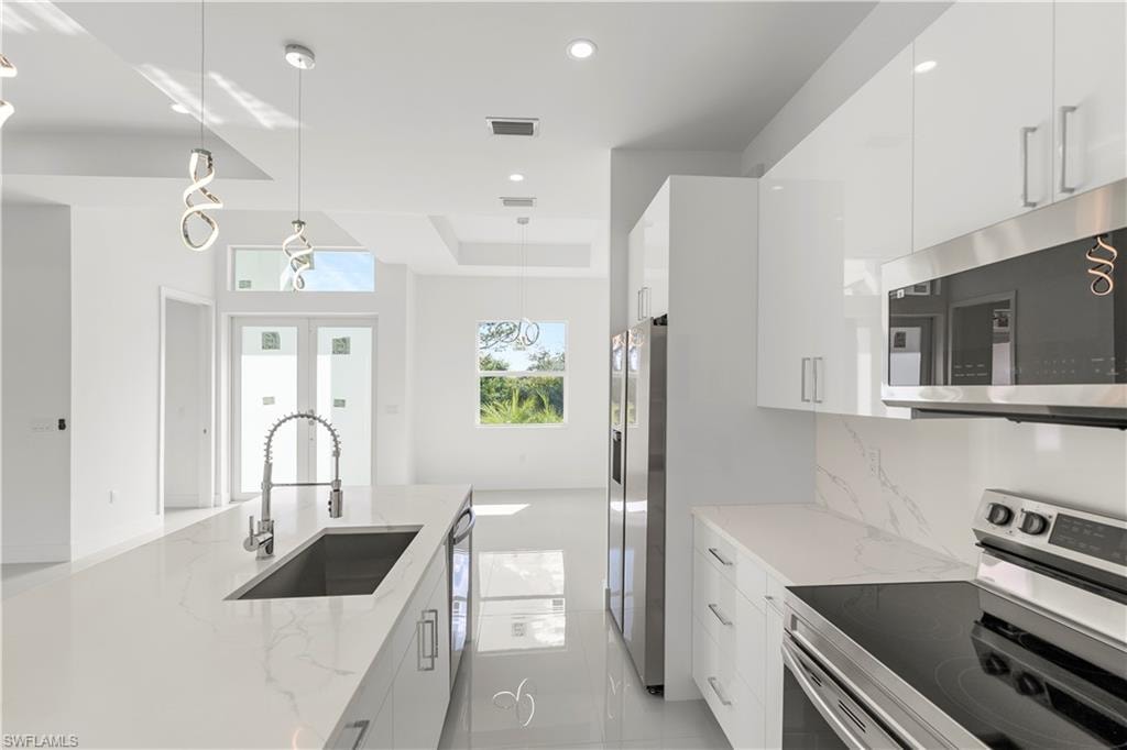 Kitchen with appliances with stainless steel finishes, hanging light fixtures, modern cabinets, light stone countertops, and recessed lighting