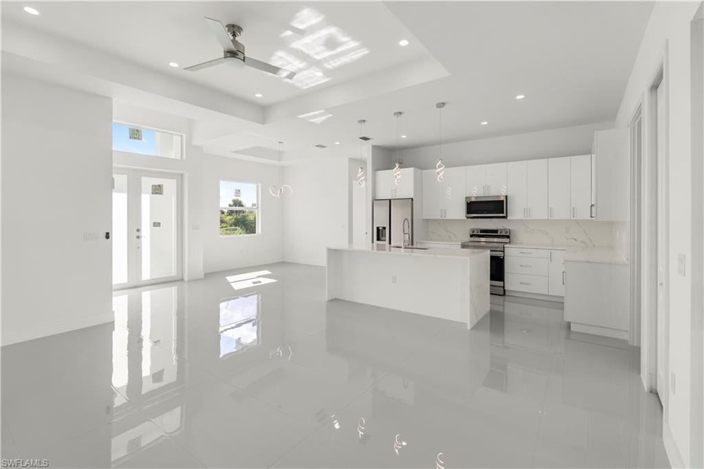 Kitchen with white cabinetry, tasteful backsplash, stainless steel appliances, hanging light fixtures, and light stone countertops