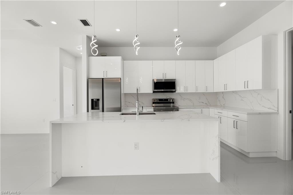 Kitchen featuring light stone countertops, hanging light fixtures, stainless steel appliances, tasteful backsplash, and white cabinetry