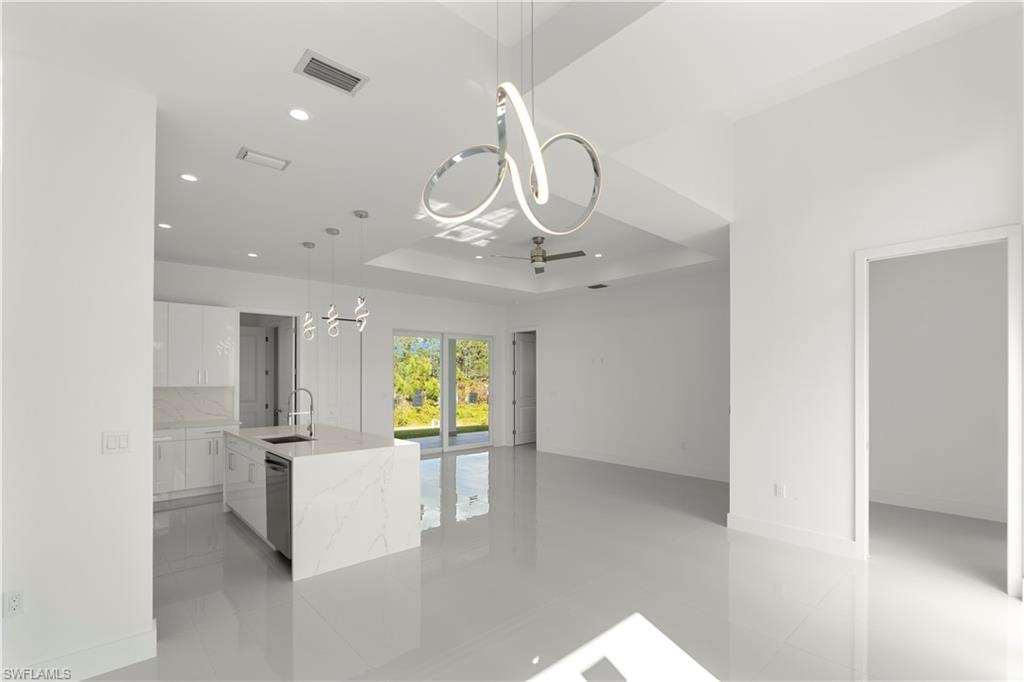 Kitchen featuring white cabinetry, a chandelier, a tray ceiling, hanging light fixtures, and light stone counters