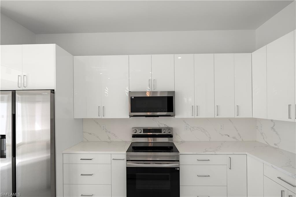 Kitchen with appliances with stainless steel finishes, white cabinets, modern cabinets, and light stone counters