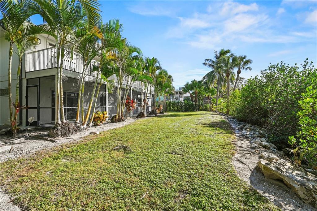 View of grassy yard with a sunroom, glass enclosure, and a balcony