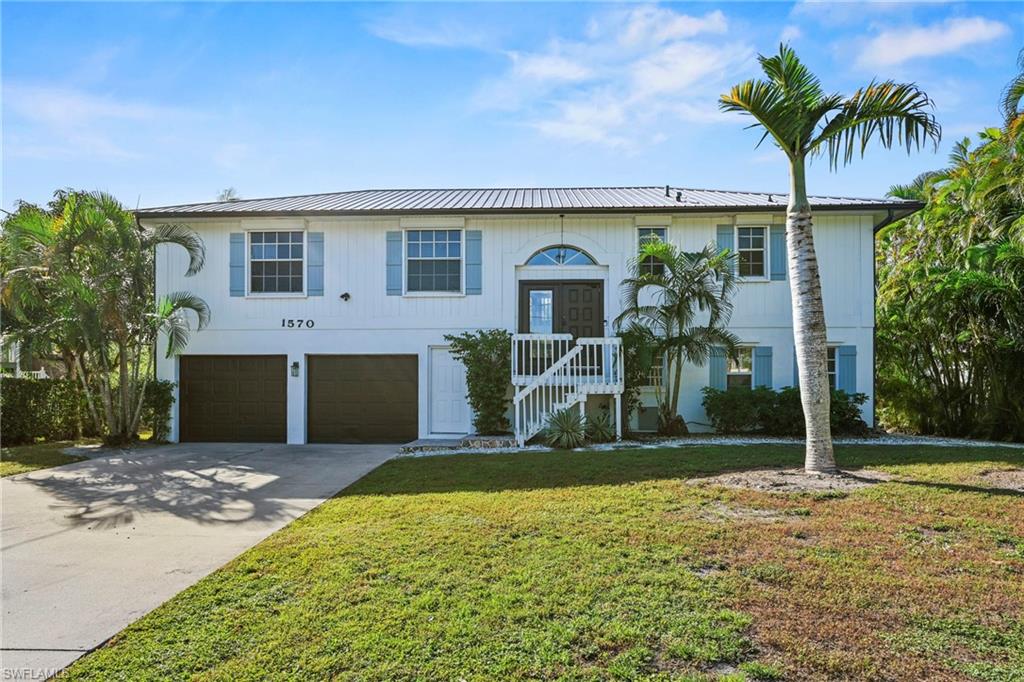 Split foyer home with concrete driveway, a garage, a metal roof, and a front yard