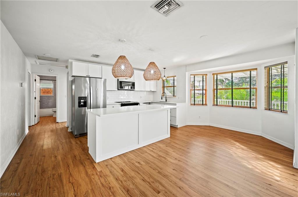 Kitchen featuring white cabinetry, decorative backsplash, a kitchen island, appliances with stainless steel finishes, and light wood finished floors