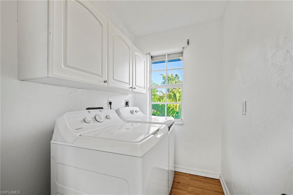 Washroom with light wood-style floors, cabinet space, washing machine and clothes dryer, and a textured wall