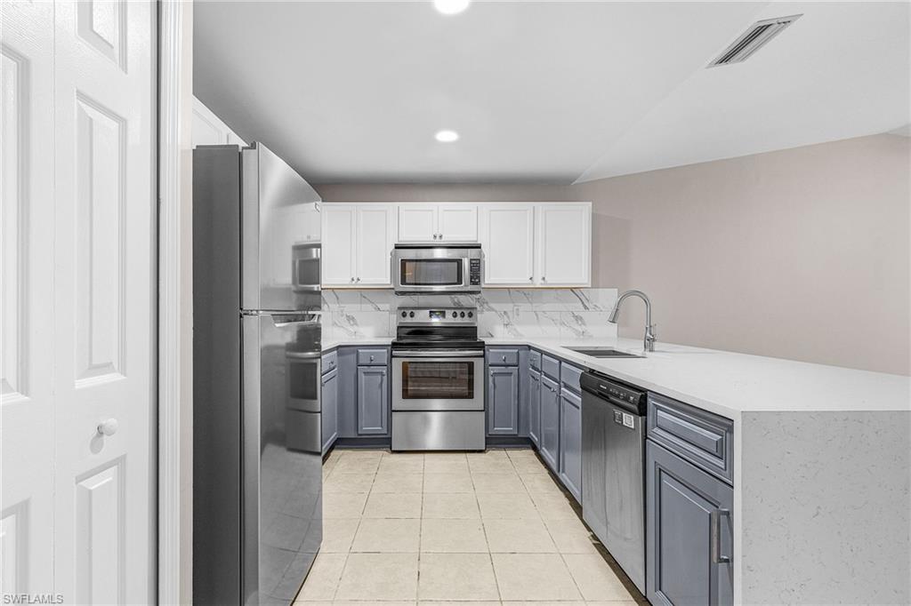 Kitchen featuring white cabinetry, appliances with stainless steel finishes, a peninsula, light stone countertops, and light tile patterned floors