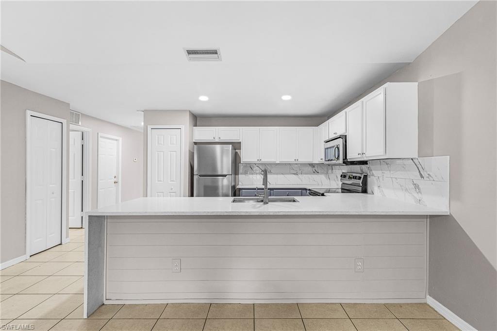 Kitchen with a peninsula, tasteful backsplash, stainless steel appliances, white cabinetry, and light stone counters