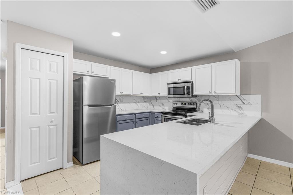 Kitchen featuring stainless steel appliances, white cabinetry, light tile patterned floors, a peninsula, and tasteful backsplash