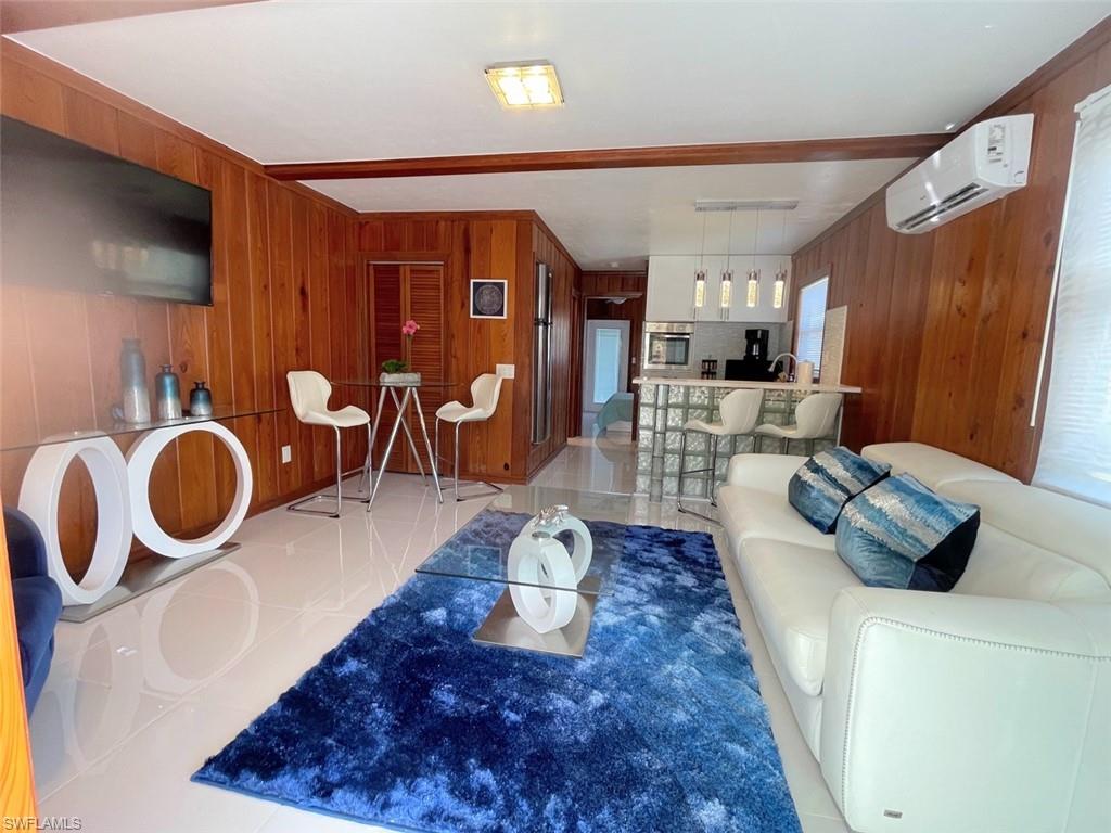 Living area featuring wooden walls, light tile patterned floors, and a wall mounted air conditioner