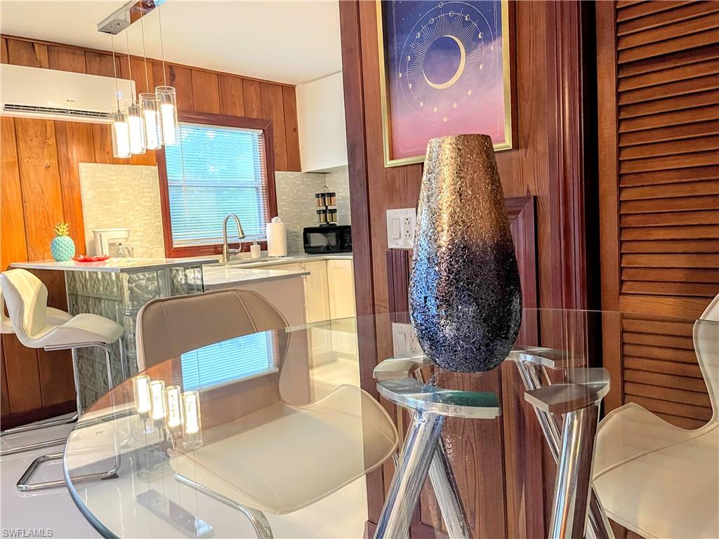 Kitchen with pendant lighting, a breakfast bar, an AC wall unit, wooden walls, and black microwave