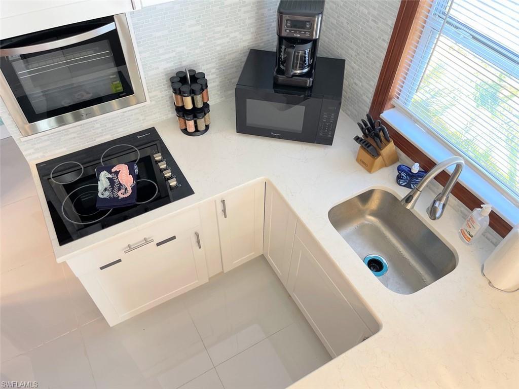 Kitchen featuring white cabinetry, black appliances, light stone counters, tile patterned floors, and backsplash