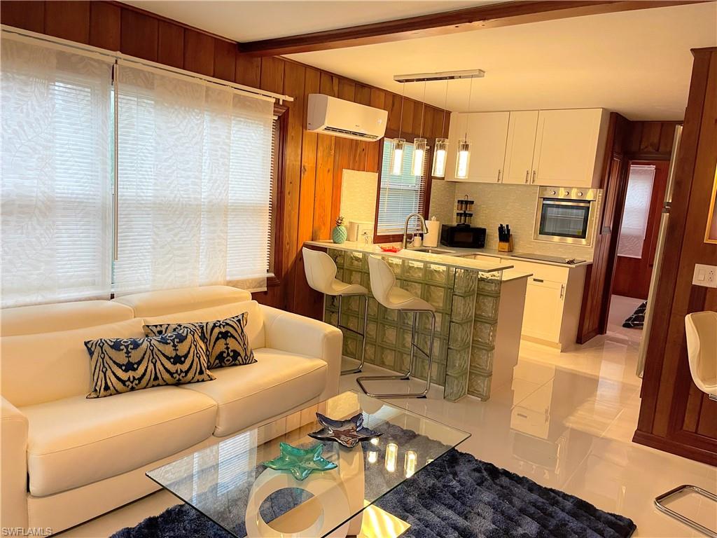 Living area with light tile patterned flooring, wooden walls, a wall unit AC, and beam ceiling
