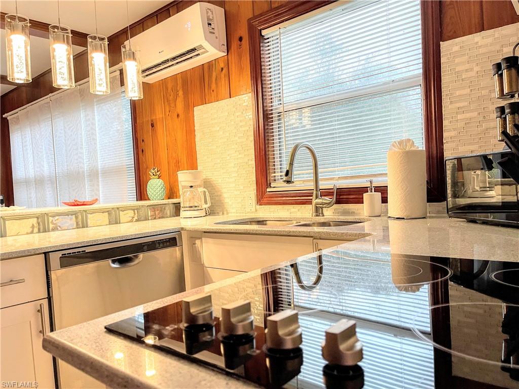 Kitchen with decorative light fixtures, black electric stovetop, light stone countertops, a wall unit AC, and stainless steel dishwasher