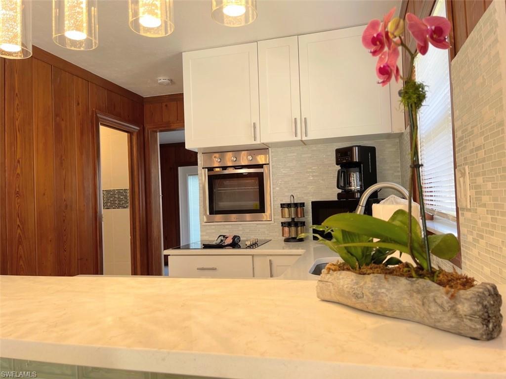 Kitchen featuring white cabinetry, oven, pendant lighting, tasteful backsplash, and light stone counters