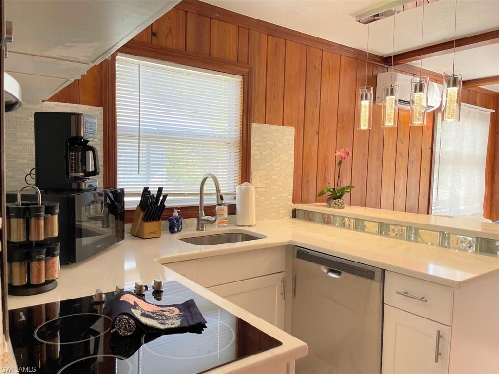 Kitchen featuring black electric cooktop, wood walls, dishwasher, decorative light fixtures, and light stone countertops