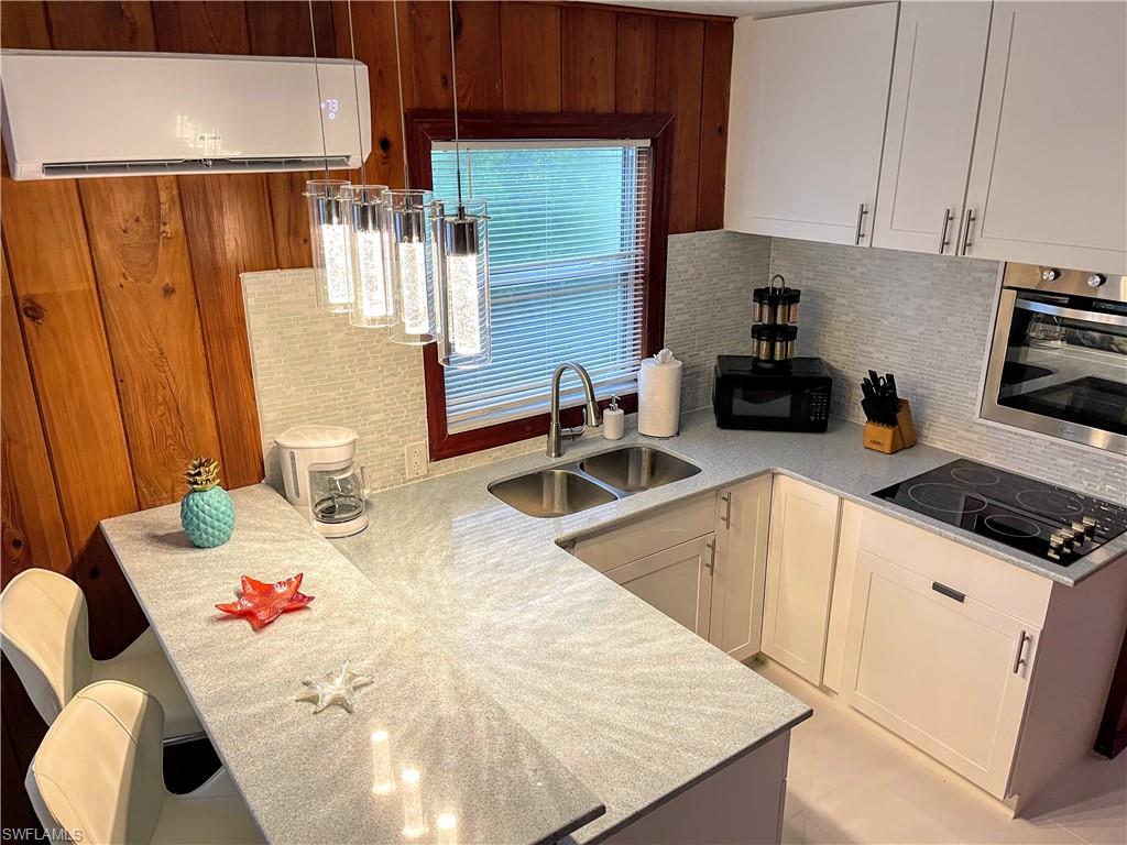 Kitchen featuring a kitchen bar, black appliances, a peninsula, light stone counters, and backsplash