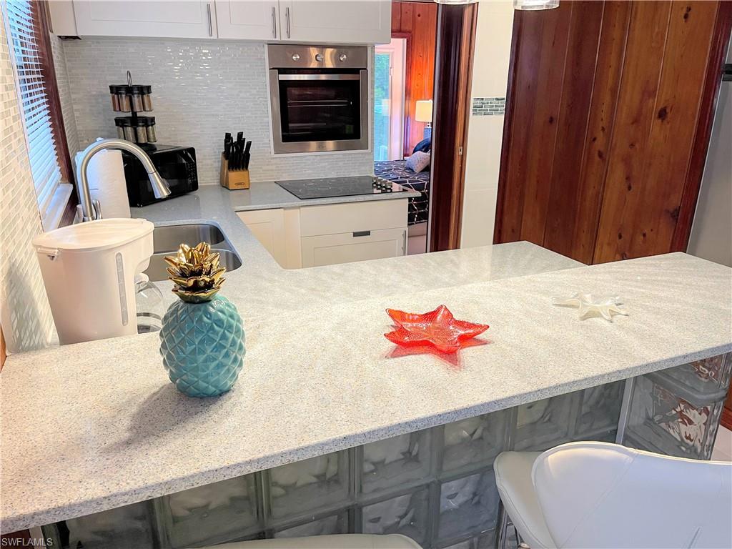 Kitchen with light stone counters, black appliances, decorative backsplash, a kitchen bar, and white cabinets