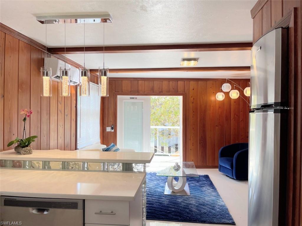 Kitchen featuring hanging light fixtures, appliances with stainless steel finishes, wooden walls, beam ceiling, and light stone counters
