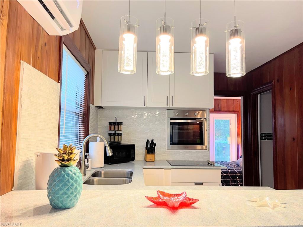 Kitchen featuring light stone countertops, oven, hanging light fixtures, white cabinets, and a wall unit AC