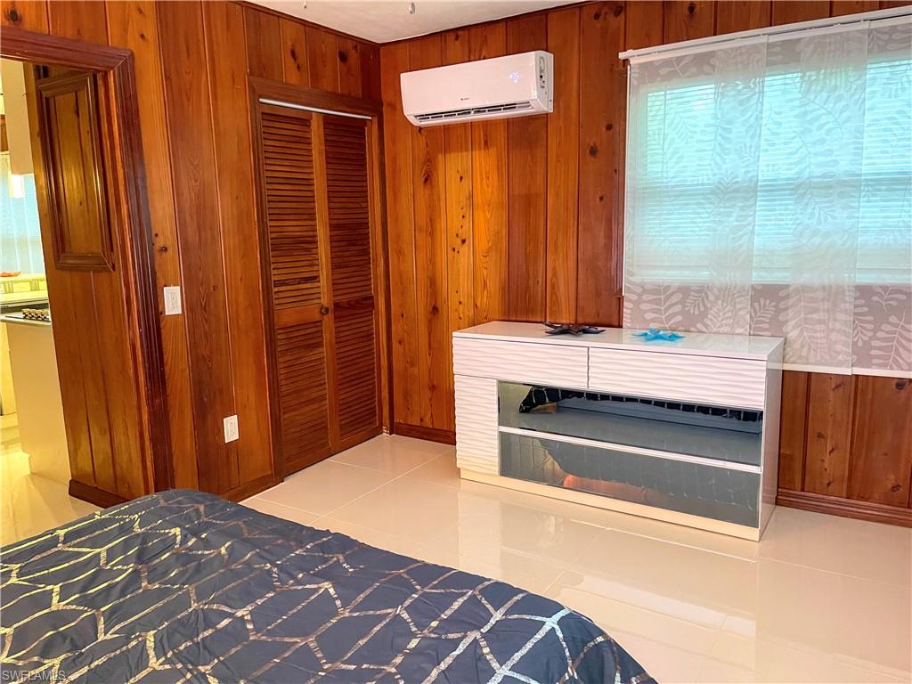 Unfurnished bedroom with wood walls, light tile patterned floors, a closet, and a wall mounted air conditioner