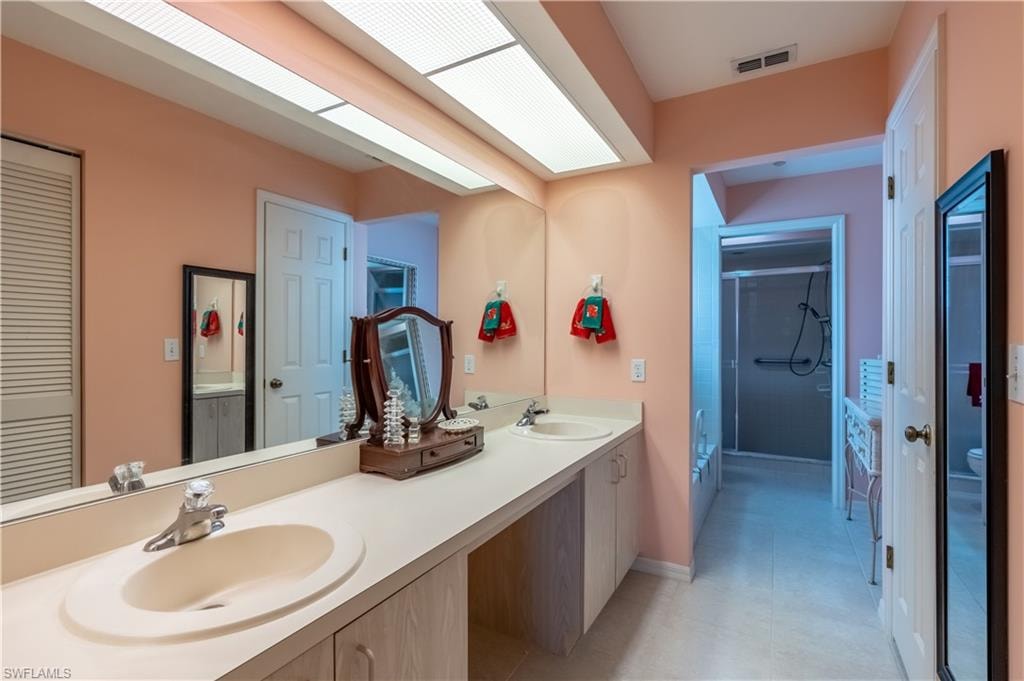 Full main bathroom featuring double vanity, dual sinks, shower stall, closet, and light tile patterned floors