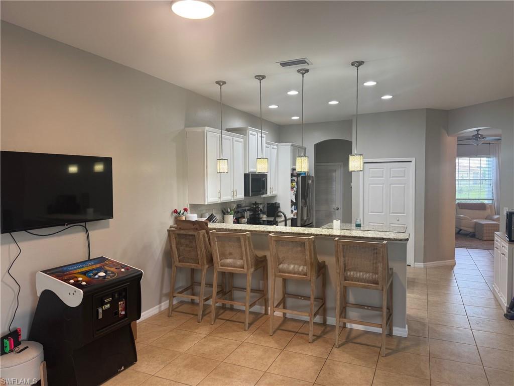 Kitchen with a breakfast bar area, white cabinetry, ceiling fan, hanging light fixtures, and recessed lighting