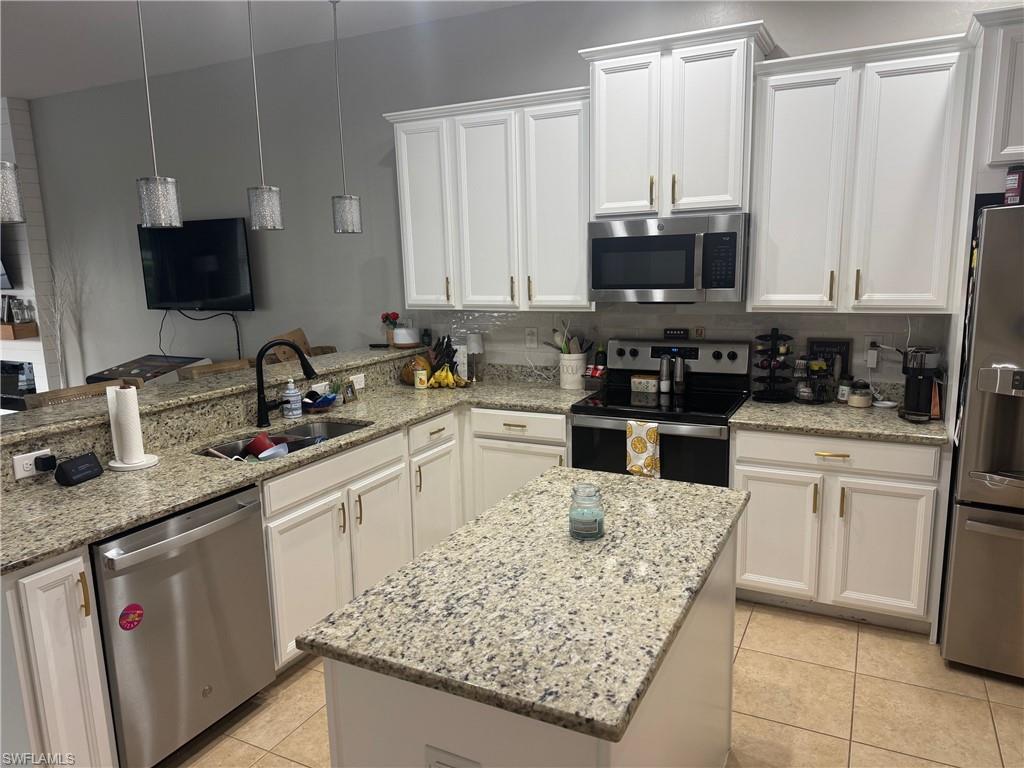 Kitchen with stainless steel appliances, white cabinetry, light stone counters, decorative light fixtures, and light tile patterned floors