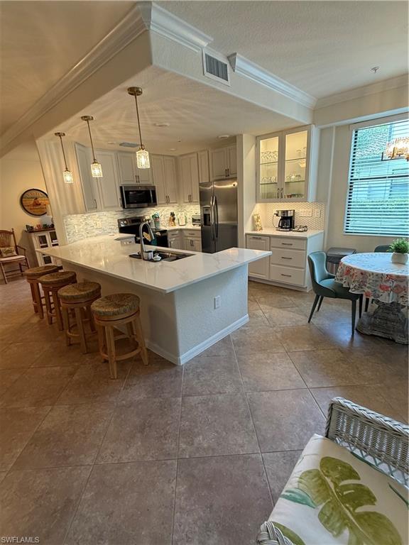 Kitchen with crown molding, tasteful backsplash, glass insert cabinets, a breakfast bar area, and appliances with stainless steel finishes