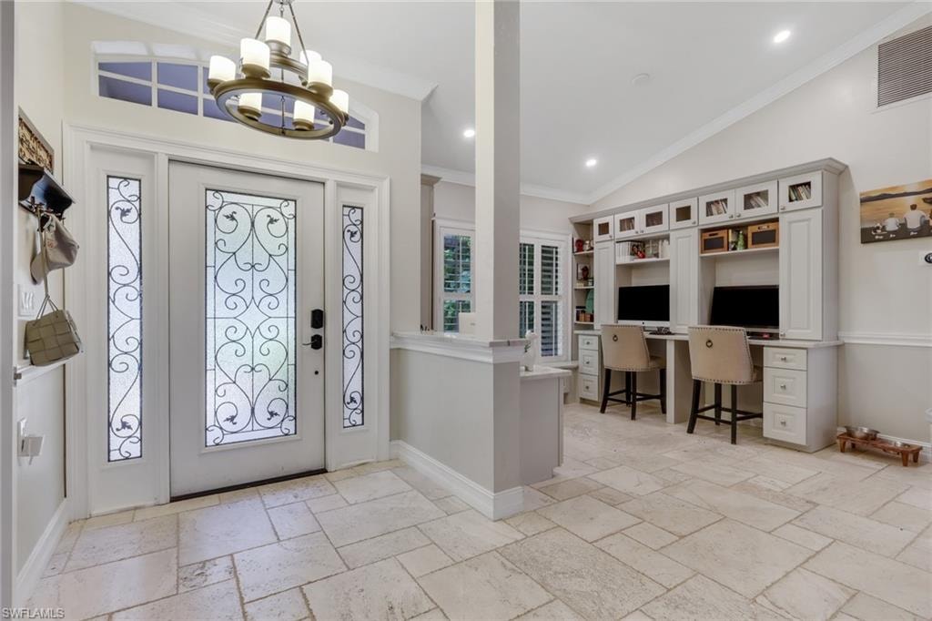 Foyer with built in desk, crown molding, stone tile flooring, lofted ceiling, and a chandelier