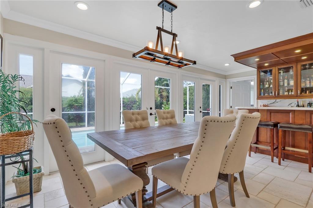Dining space featuring ornamental molding, french doors, recessed lighting, a bar, and stone tile flooring