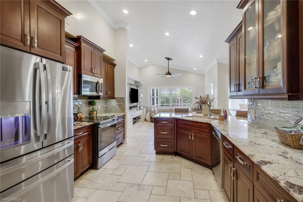 Kitchen with tasteful backsplash, appliances with stainless steel finishes, crown molding, a peninsula, and light stone countertops