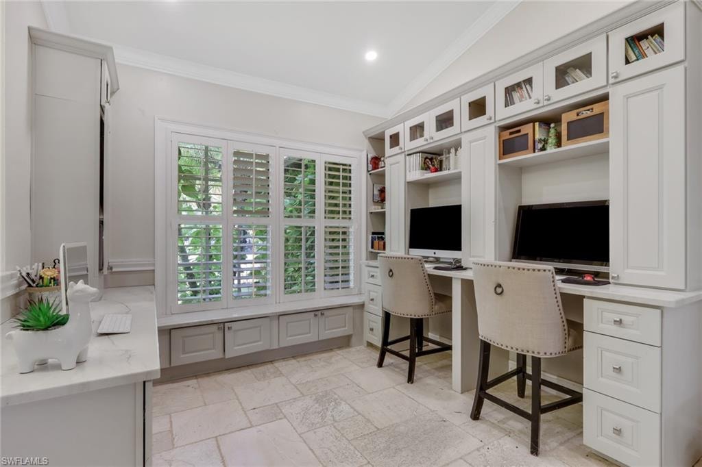Office area featuring built in desk, ornamental molding, stone tile flooring, lofted ceiling, and recessed lighting